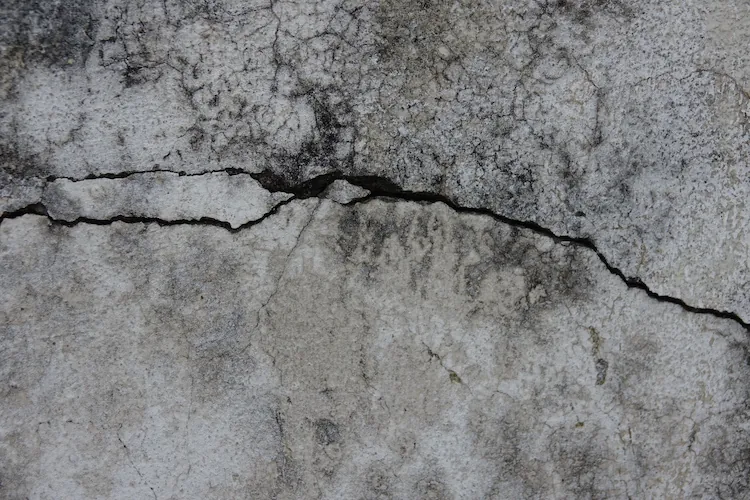 Close-up of a long diagonal crack running across a weathered concrete retaining wall